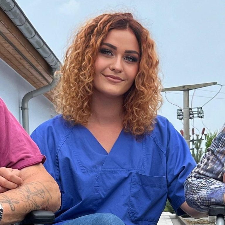 Frau mit blonden Haaren und Brille, am Telefon, trägt T-Shirt mit Erdbeeren.