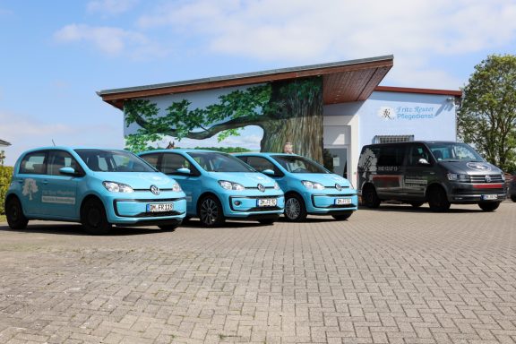 Vier Autos, drei hellblau und ein dunkelgrau, stehen vor einem modernen Gebäude.
